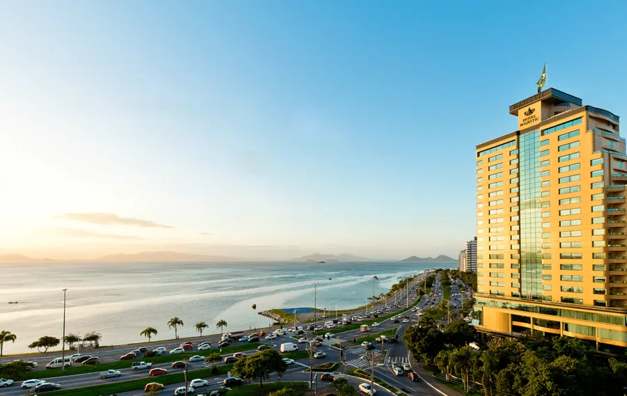 Hotel Majestic Palace na Avenida Beira-Mar Norte, ao entardecer, com a baía e os morros ao fundo.